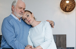 An older man in a blue sweater consoling a woman in a white blouse